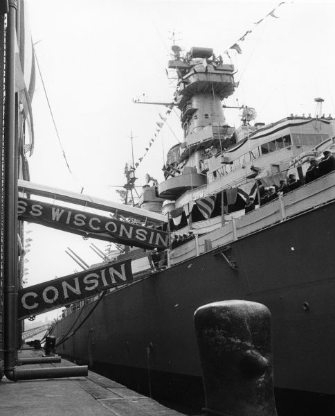 View of the U.S.S. <i>Wisconsin</i> docked during decommissioning ceremonies in preparation for its final cruise. A number of sailors can be seen on deck.