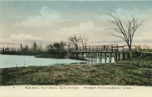 View of a wooden bridge spanning the Bark River. Probably late fall or early spring as the trees are leafless. Caption reads: "Bark River Bridge, Fort Atkinson, Wis."