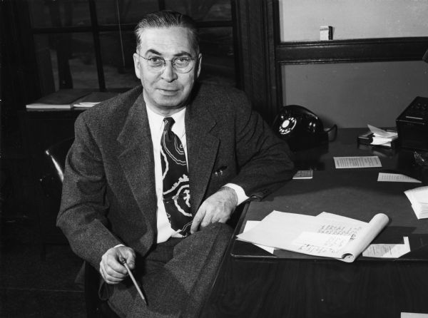 George Watson, Superintendent of Public Instruction in Wisconsin, seated at his desk wearing a necktie and holding a pencil.