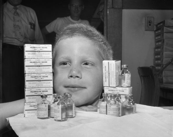 Child posing with polio vaccine bottles and boxes.