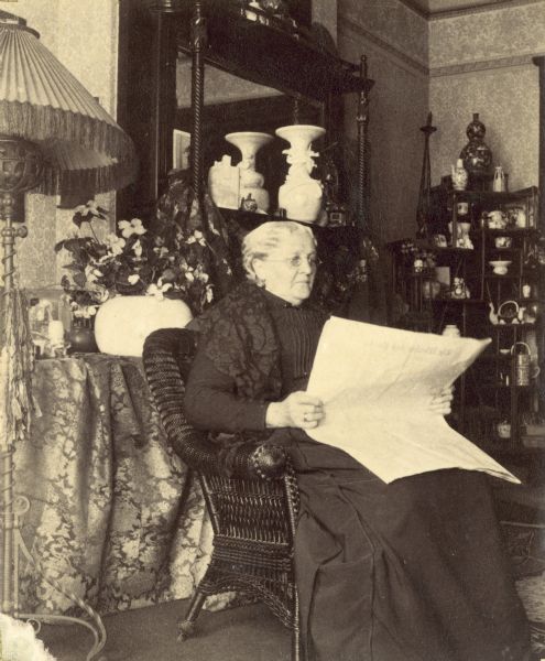 "Aunt Li de Scidmore" is seated in a chair reading a newspaper.