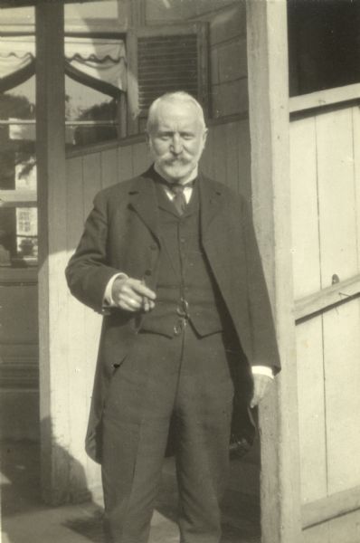 George Hawthorne Scidmore stands outdoors wearing a suit and holding a cigar.