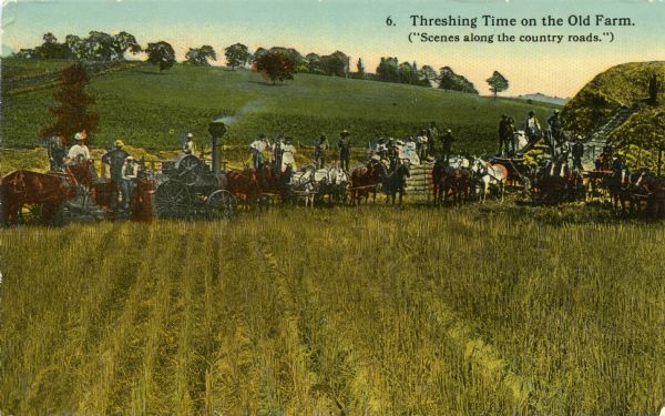 Hand-colored postcard showing a farm crew with horses, a tractor, and other agricultural implements threshing grain crops in a field. Women in dresses pose with the men in the field.