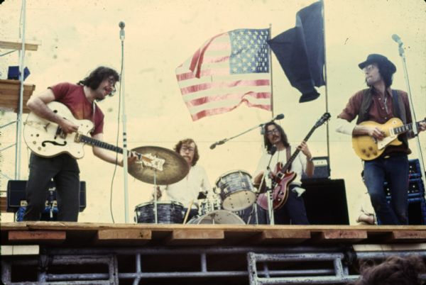 Wilderness Road performing on stage at Sound Storm. On guitar at left is Nate Herman, Tom Haban on drums, Andy Haban on bass, and Warren Leming on guitar at right. The band flew a U.S. flag and a black flag during their performance.
