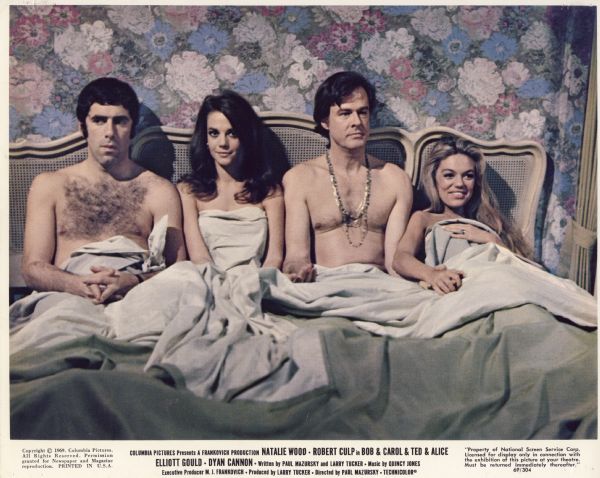 Color scene still from the Columbia film "Bob & Carol & Ted & Alice," featuring Elliott Gould (playing Ted Henderson), Natalie Wood (playing Carol Sanders), Robert Culp (playing Bob Sanders), and Dyan Cannon (playing Alice Henderson) who are all in bed together.
