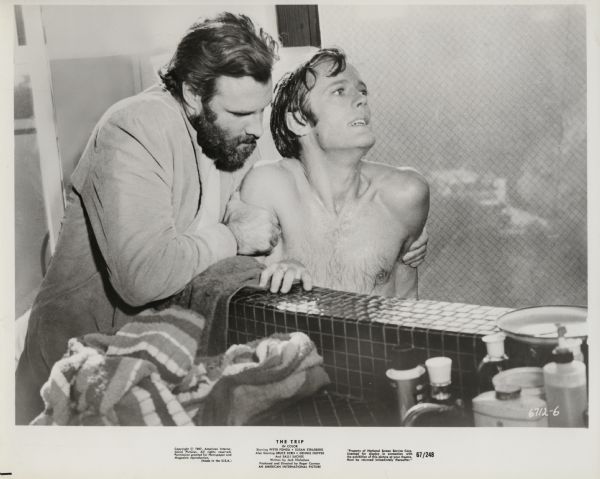 Scene still from the American International film "The Trip," featuring Bruce Dern (playing John) and Peter Fonda (playing Paul Groves). Dern's character (in a full beard) is helping Fonda's character, who is in a bathtub, as he trips on L.S.D.