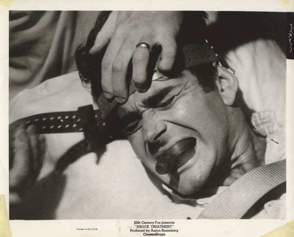Movie still from the Twentieth Century-Fox film "Shock Treatment," featuring Stuart Whitman (playing Dale Nelson) who is shown undergoing electroshock treatment clenching a rubber mouthpiece betweenn his teeth.