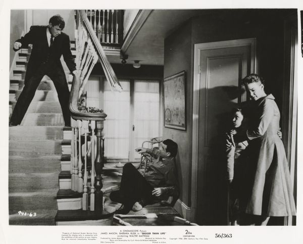 Dramaic scene still from the Twentieth Century-Fox movie "Bigger Than Life," featuring Walter Matthau (playing Wally Gibbs), James Mason (playing Ed Avery), Christopher Olsen (playing Richie Avery), and Barbara Rush (playing Lou Avery). Ed Avery and Wally Gibbs are fist fighting while Avery's wife and son cower against a wall.