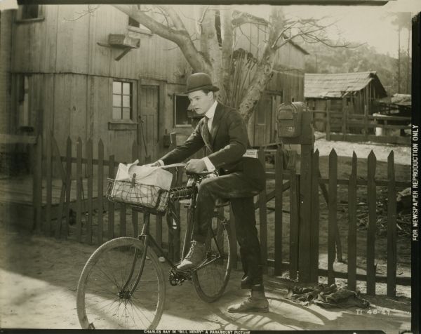 Scene still from the Paramount silent film "Bill Henry," featuring Charles Ray (playing Bill Henry Jenkins) setting off on his bicycle to begin his new job as a traveling salesman. A copy of the book "The Knack of Selling" is in his pocket.