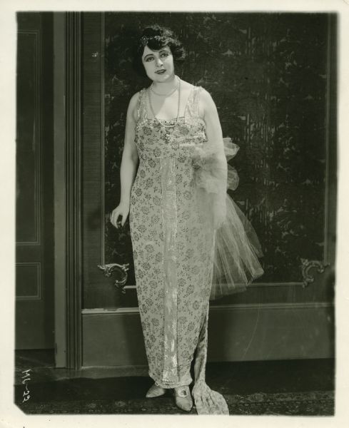 Movie still from the Fox movie "The Tattlers," featuring Madlaine Traverse (playing Bess Rutherford) posing in an evening dress.