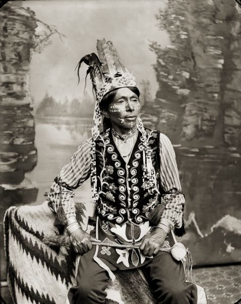 Portrait of Branching Horns, a Ho-Chunk man, posing in front of a painted backdrop.