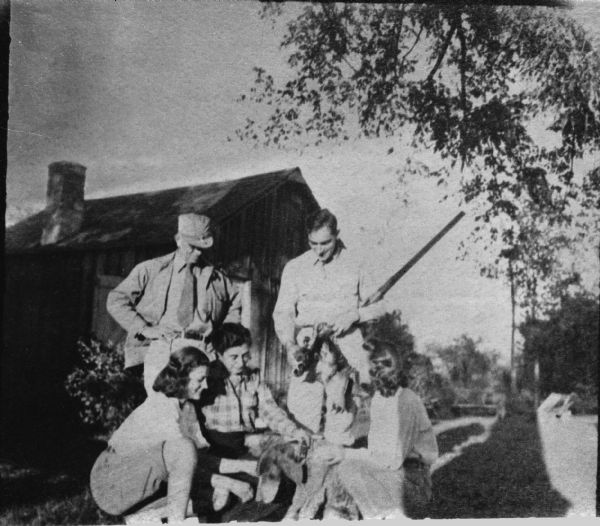 Caption on negative sleeve: "Aldo Leopold and son Luna (standing); Mrs. Leopold and two daughters Nina and Estella (kneeling). 'Shack' in background." The women are petting a dog.