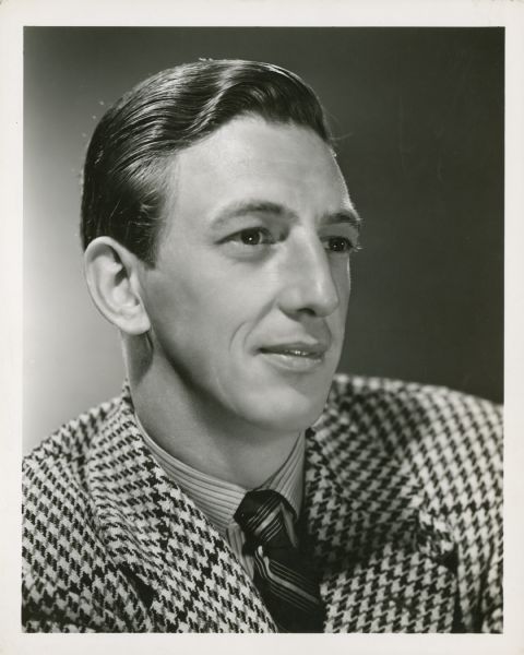 Publicity still of actor Ray Bolger in a checkered suit jacket. Photographed by Clarence S. Bull. Caption reads: Ray Bolger... Latest portrait of the eccentric dancer, appearing in a leading comedy role in Metro-Goldwyn-Mayer's "Sweethearts," with Jeanette MacDonald and Nelson Eddy. W.S. Van Dyke II directs, with Hunt Stromberg producing in Technicolor.