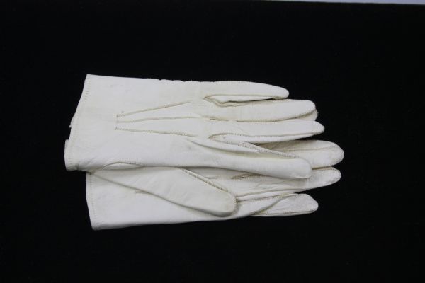 These girl's gloves are made of off-white kid leather. They are completely hand-stitched in beige thread, top stitched around the fingers and thumb, with three rows of top stitching down top of hand. There is an elaborate dark metal hook and eye closure at wrist, with tiny etchings in the metal. Blue pencil markings inside right glove indicate the original sewing pattern. Matching markings in the left glove, including the words "M. Courvoisier."