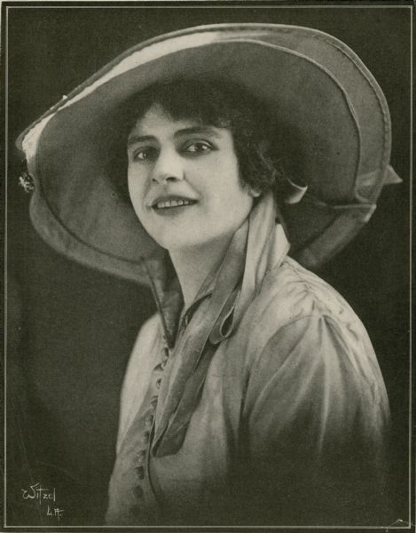 Publicity photograph of Helen Gibson from a magazine. She is wearing a dress and wide brimmed hat.
