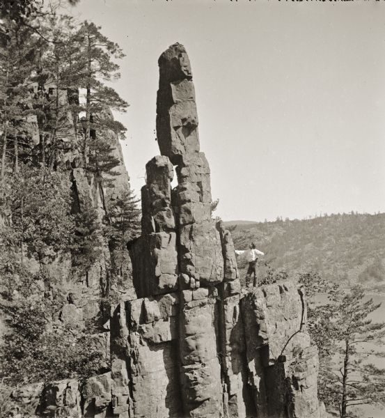 Devil's Lake Vicinity; Cleopatra's Needle in Wonder Notch. There is a man standing on a rock outcropping beside the Needle.
