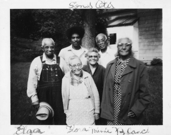 A group portrait taken at the home of Alga Shivers. In front, from left to right, are: Alga Shivers (in overalls), his wife Flora Shivers, Minnie Drake, and Blanche Arms. In back from left to right are the Arms' son and Otis Arms.