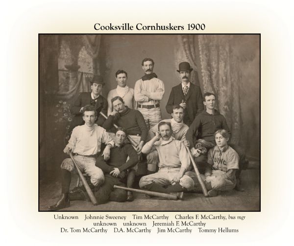 Names have been added to this group portrait of Cooksville Cornhuskers baseball team in front of a painted backdrop. Top left to right: Unknown, Johnny Sweeney, Tim McCarthy(?), Charles F. McCarthy. Middle section: Unknown, Unknown, Jeremiah McCarthy. Front Row: Dr. Tom McCarthy, D.A. McCarthy, Jim McCarthy and Timothy Hellum.