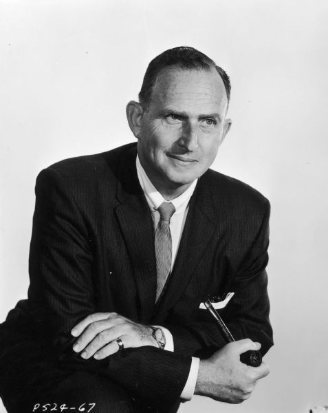 Indoor portrait of Lewis Rachmil, the producer of the television show <i>Men Into Space</i>. He is wearing a suit and is leaning on his knee and holding a pipe.