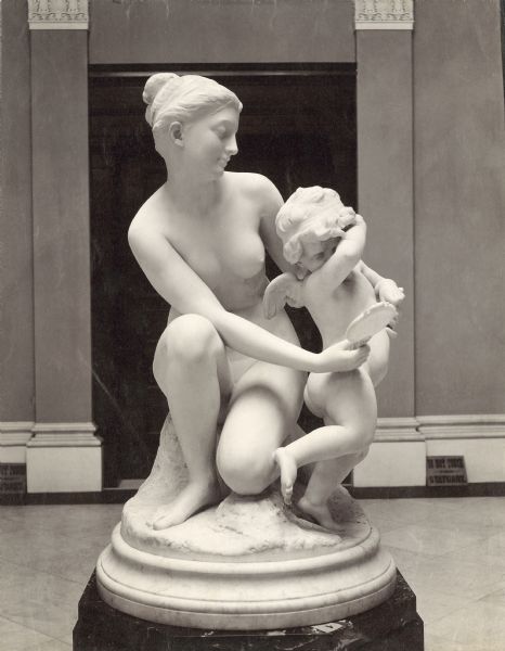A sculpture of a woman and baby on exhibit, entitled <i>Rebellion</i>. The sculpture depicts the woman trying to show a baby, who is hiding his eyes, his reflection in a hand mirror.
