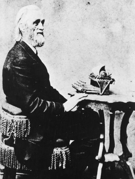 Portrait of Christopher Latham Sholes posing at a typewriter.