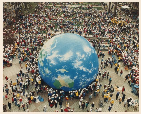 Elevated view of a large crowd of people wearing hard hats gathered on the National Mall. They are building a huge model of the planet Earth for the 25th Anniversary celebration of Earth Day.