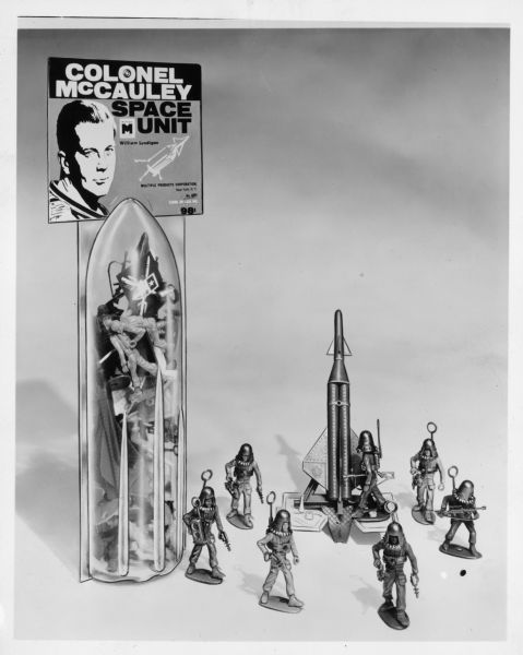 Display of toys. On the left is the Colonel McCauley Space Unit, which includes a clear plastic container shaped like a rocket holding action figures. There is also a missile, and more action figures dressed and equipped to fight in space.