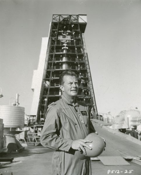 William Lundigan, who stars as Colonel Ed McCauley on the television show <i>Men into Space</i>, stands outdoors in front of a missile or rocket launch pad.
