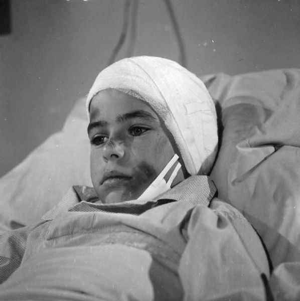 A young boy in the hospital bed with his head and chin bandaged in a scene from the television show <i>Men Into Space</i>.