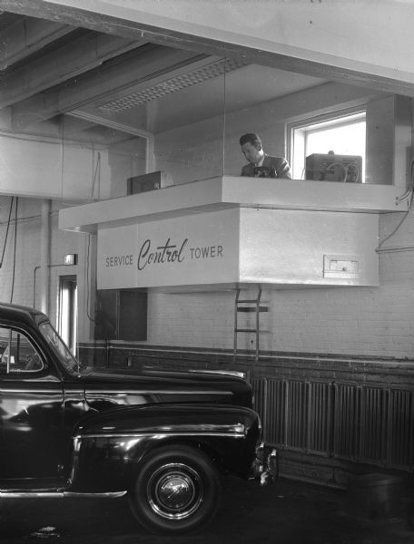 Service control tower in the service department of Kayser's Motors, 701 East Washington Avenue. A service manager is shown in the suspended tower and a truck is in the left foreground.