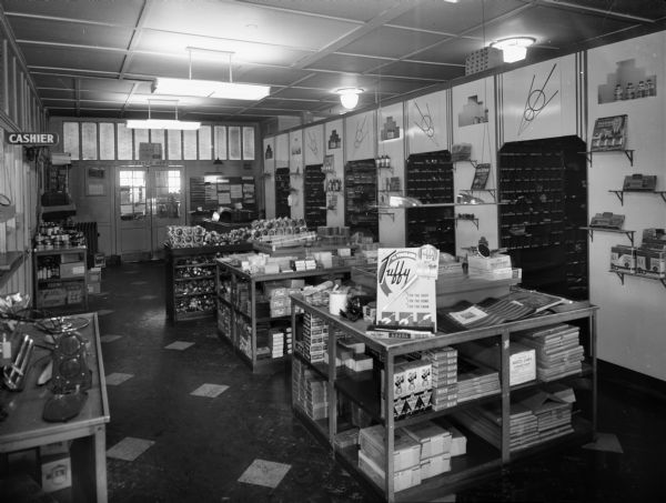 Slightly elevated interior view of the stockroom at Kayser Motor Inc., 701 East Washington Avenue, showing display tables and stocked shelves.
