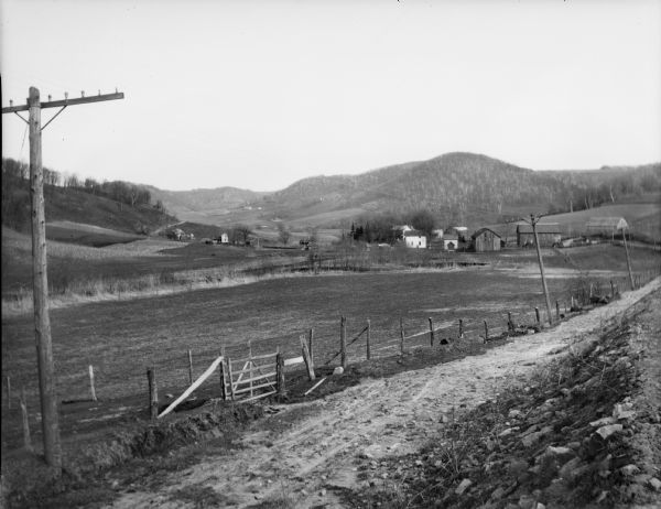 View across dirt road of farms and farm buildings in a valley.