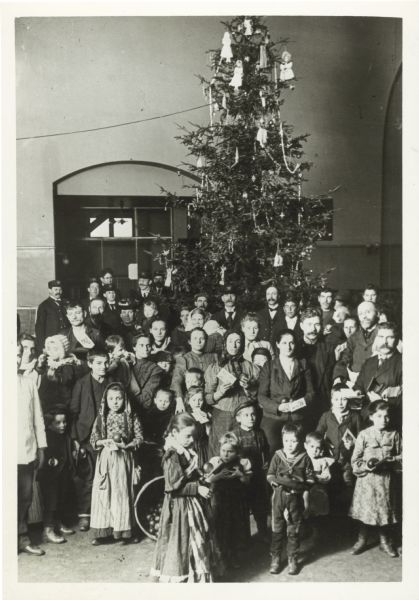 A group of immigrants pose in front of a tall Christmas tree at Ellis Island.