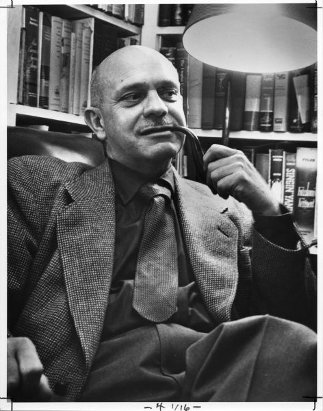 Informal portrait of William Hesseltine, University of Wisconsin  History Professor (1932-1963) and President of the Wisconsin State Historical Society (1961-1963)seated in front of a bookshelf and smoking a pipe.  He died at age 61 in Dec. 1963.