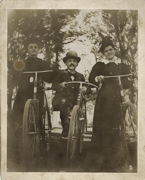 Two women and one man posing outdoors, each holding a bicycle. The man is identified as Dennis Baird.