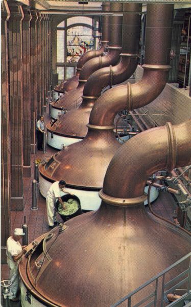 Postcard of the Pabst Brewery showing an elevated view of men working near the copper kettles in a vaulted room. There is a large, stained glass window on the wall in the background.