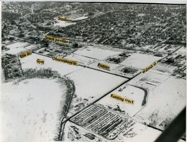 Aerial view of the UW-Madison campus near University Bay in winter. Labels are pasted to the print to indicate Elm Dr., the gym, Camp Randall Stadium, the Stock Pavilion, Observatory Dr., the Biotron, Walnut St., and the running track.