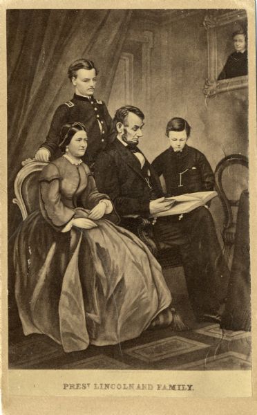 Portrait of Abraham Lincoln and family. The President is reading to his son Thomas (Tad) with Mary Todd seated at his side and son Robert standing behind them. A portrait of the Lincolns' son William, who died in 1862 while the family lived in the White House, hangs at right. The portrait is a composite image created using a Matthew Brady photograph of Abraham Lincoln reading to Thomas.