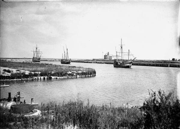 View from shoreline of replicas of Columbus' ships the Niña, the Pinta, and the Santa Maria sailing into dock at Chicago's Jackson Park.