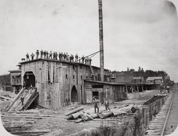 Men pose on top of and in front of the Spaulding, Van Hoosier & Company Sawmill.