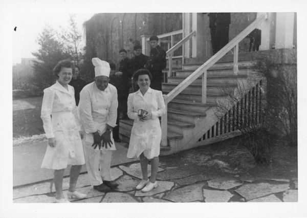 Beulah Dahle, Carson Gulley and Margaret Roeckel Miner standing in front of Van Hise Hall (now Carson Gulley Hall). Gulley is wearing his white chef uniform with a hat, and the women are wearing white dress uniforms and shoes. 

Carson Gulley Hall). The men in the background are Navy personnel. This photo was taken between 1942-44 when the The U.S. Navy ran a Cooks and Bakers School during World War II at Van Hise Hall, University of Wisconsin, for which Gulley was an instructor.