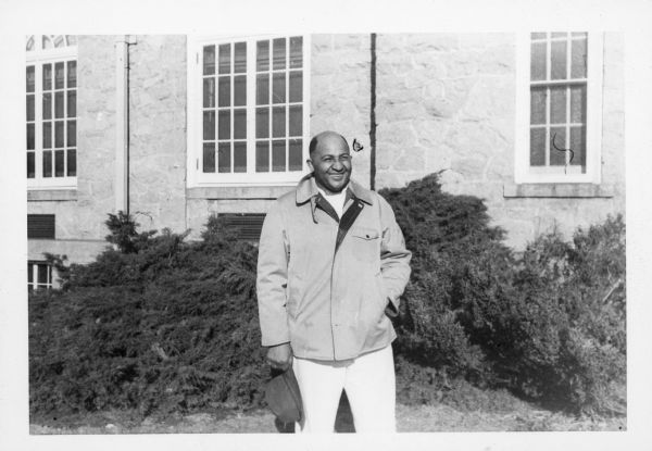 Carson Gulley stands in front of the Van Hise building on the UW-Madison campus, holding his hat in one hand, with his other hand in his jacket pocket.