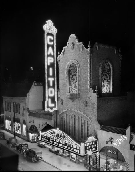 Elevated view of the Capitol Theatre at night with sign and marquee, located at 209-211 State Street. On the left is the Fred W. Kruse Co., and on the right is the Peoples Clothing Co. store.