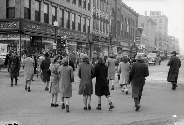 Christmas shoppers crossing the street (walking away from the photographer) at the corner of King Street on the Capitol Square in front of Kresge's, 25-27 East Main Street.