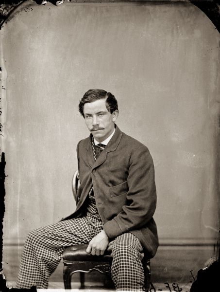 Studio portrait of Henry H. Bennett seated, wearing a suit jacket and checkered pants.
