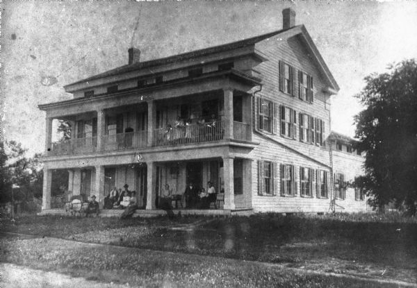 View from road of the exterior of Wade House. Children and adults are posing sitting and standing on the porch and balcony.