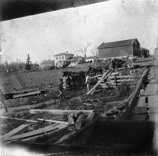 Rudolf Herrling farm looking west from the sawmill platform. Three men are near horses and carts in a fenced-in area. In the background is the farmhouse.