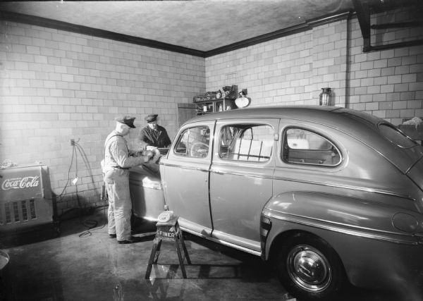 Two men "simonizing" an automobile. Photographed for the Simonize Company of Chicago. A refrigerator for Coca-Cola products is in the back of the garage.
