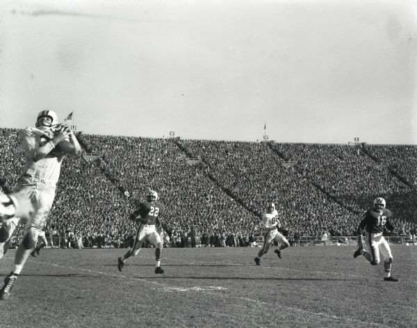 A Minnesota player leaps to catch a pass as Badger defenders approach from upfield in a game at Camp Randall Stadium. A large crowd is in the stands in the background. #22 is Sidney Williams, 1st African-American to start at quarterback in big 10 football history.