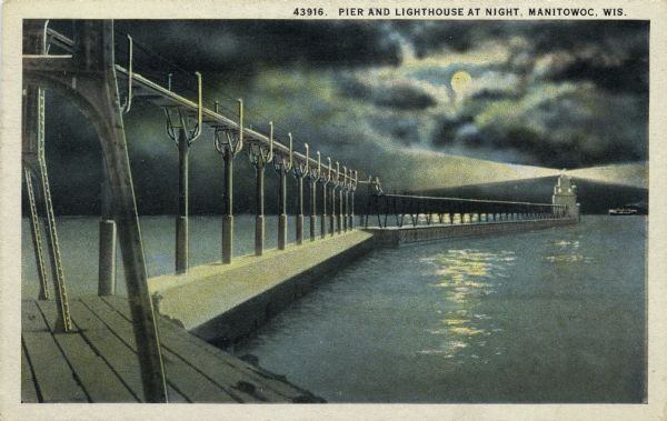 Hand-colored postcard view of a pier and lighthouse at night. The moon shines through clouds, and light shines in two directions from the beacon on top of the lighthouse. A ship is on the horizon. Caption reads: "Pier and Lighthouse at Night, Manitowoc, Wis."